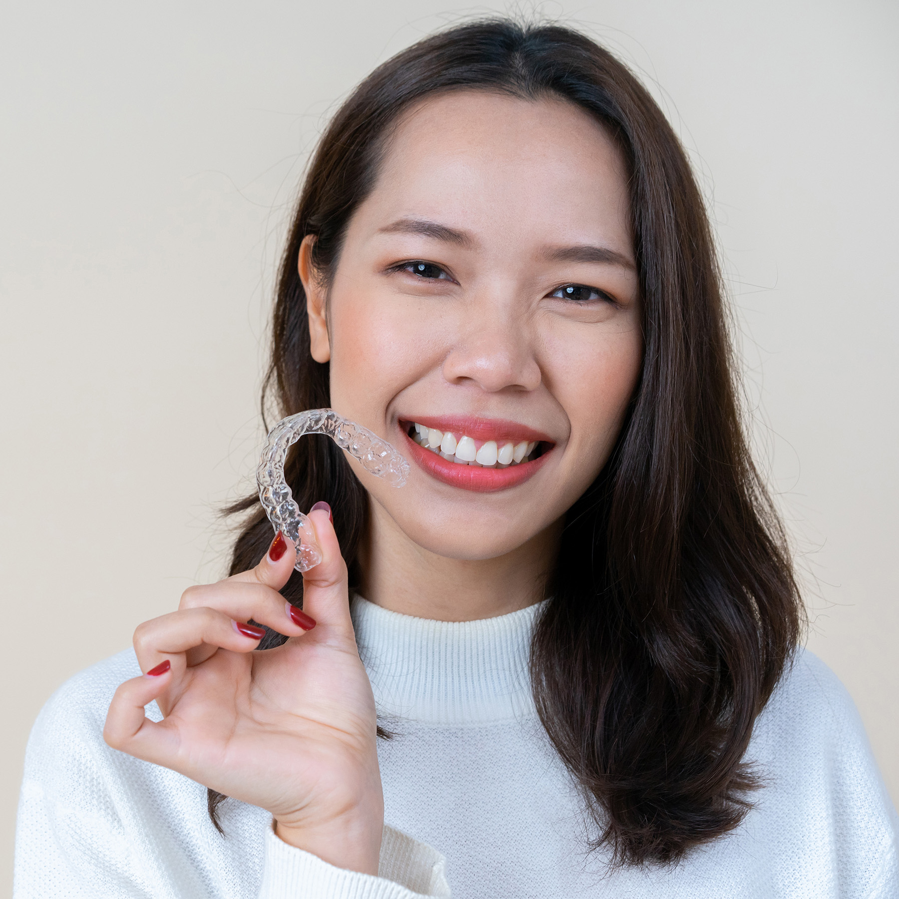 A woman holding up a clear plastic object, possibly a dental appliance or an orthodontic device, with a smile on her face.